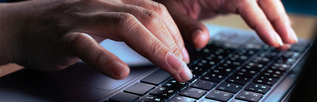 Hands typing on a laptop, illustrating the growing threat of AI-powered impersonation scams. 